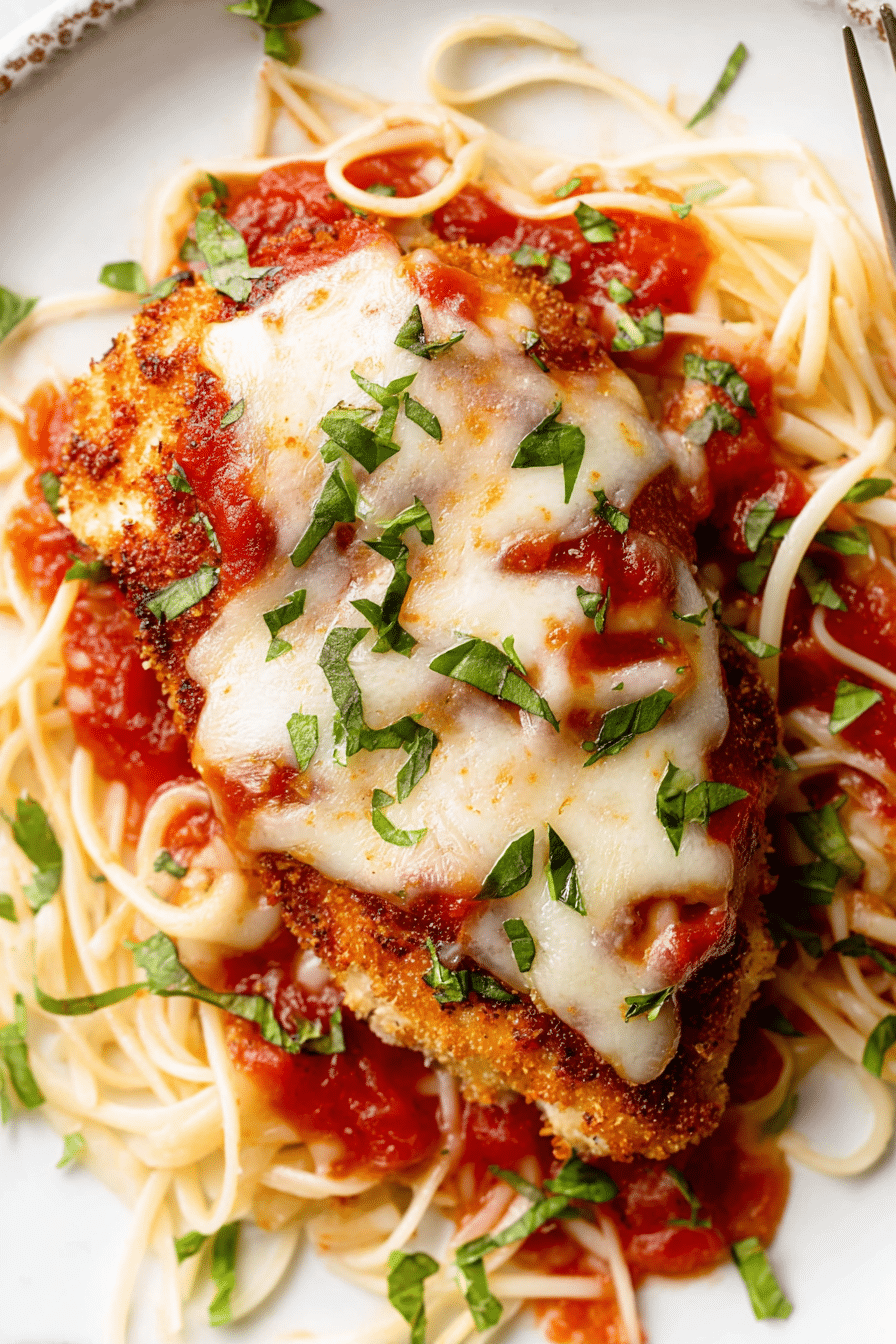 Delicious baked chicken parmesan garnished with basil, served on a wooden table.