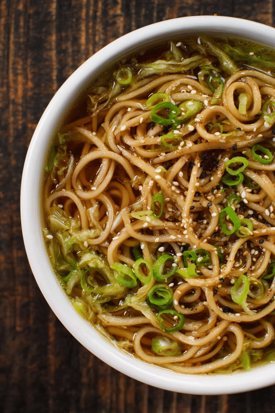 Bowl of cabbage ginger noodles topped with sesame seeds and scallions on a wooden table.