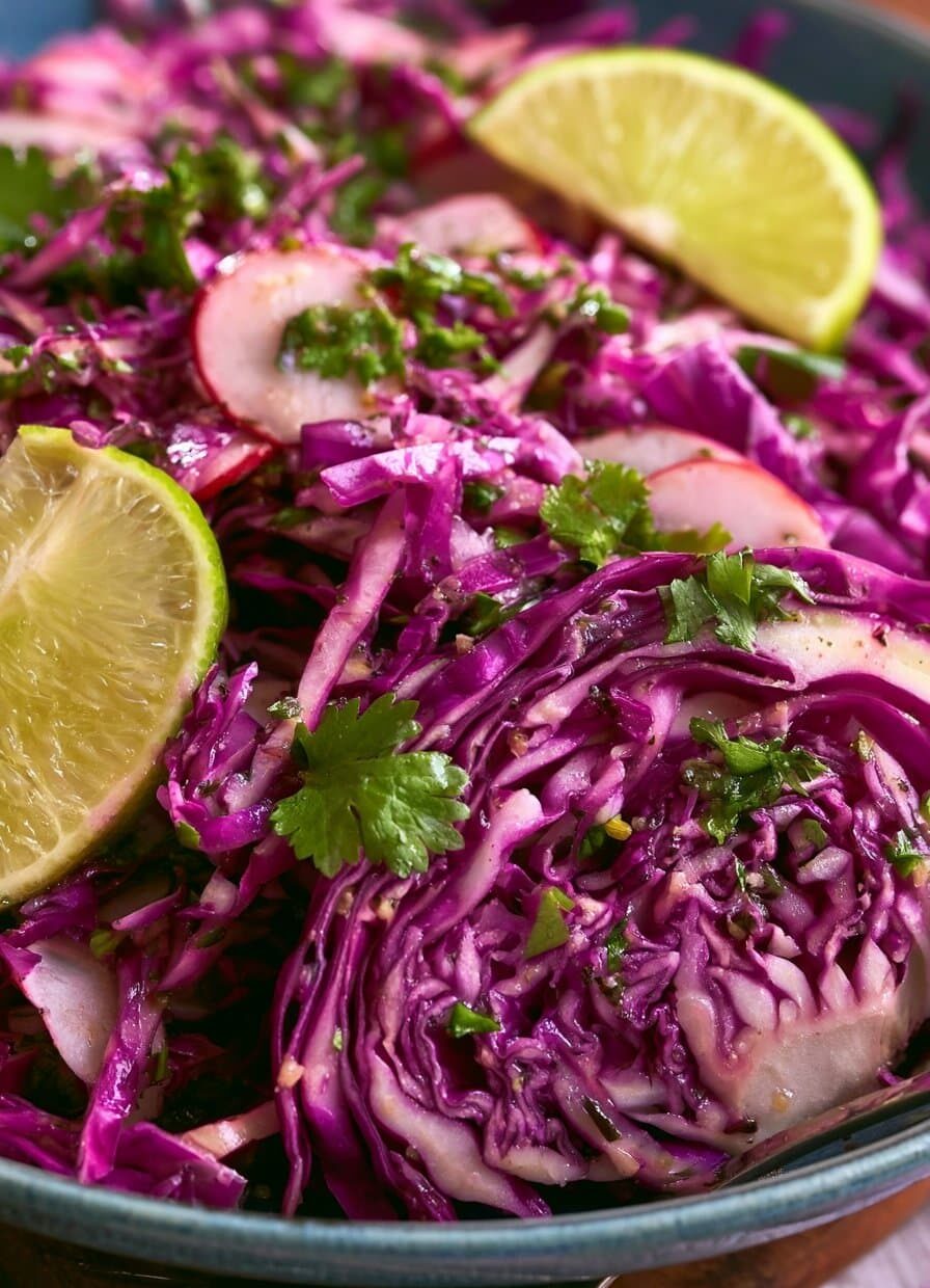 A colorful cabbage-radish slaw with cilantro-lime vinaigrette served in a wooden bowl, showcasing green and savoy cabbage, watermelon radishes, and fresh cilantro.