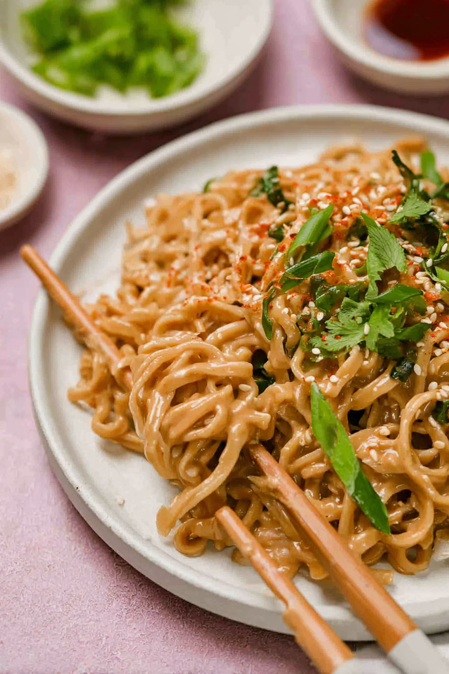 Colorful bowl of cold spicy peanut sesame noodles topped with scallions and sesame seeds.