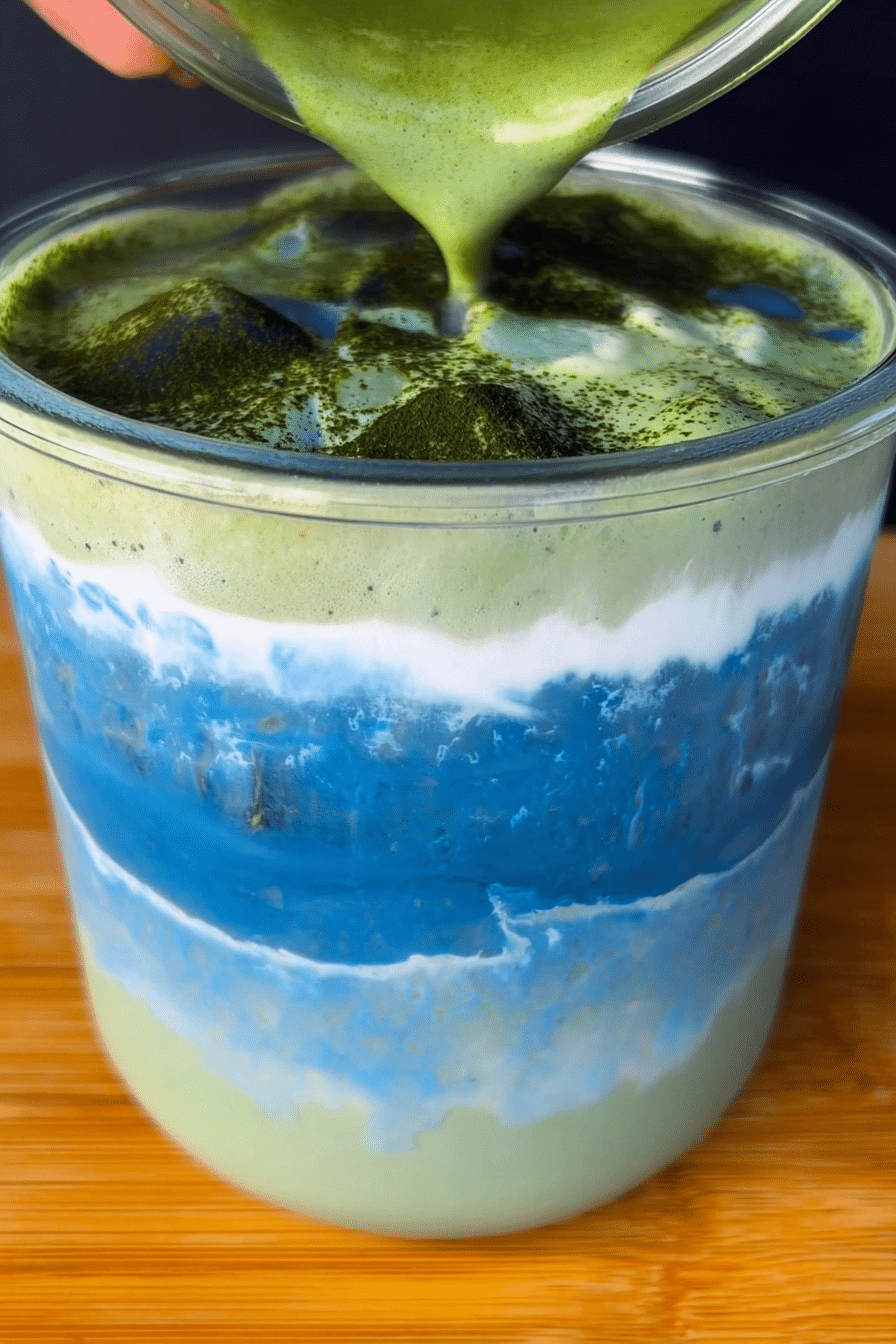 Colorful Earth Day matcha recipe featuring a layered iced latte with blue spirulina and matcha, garnished with fresh flowers and greenery.