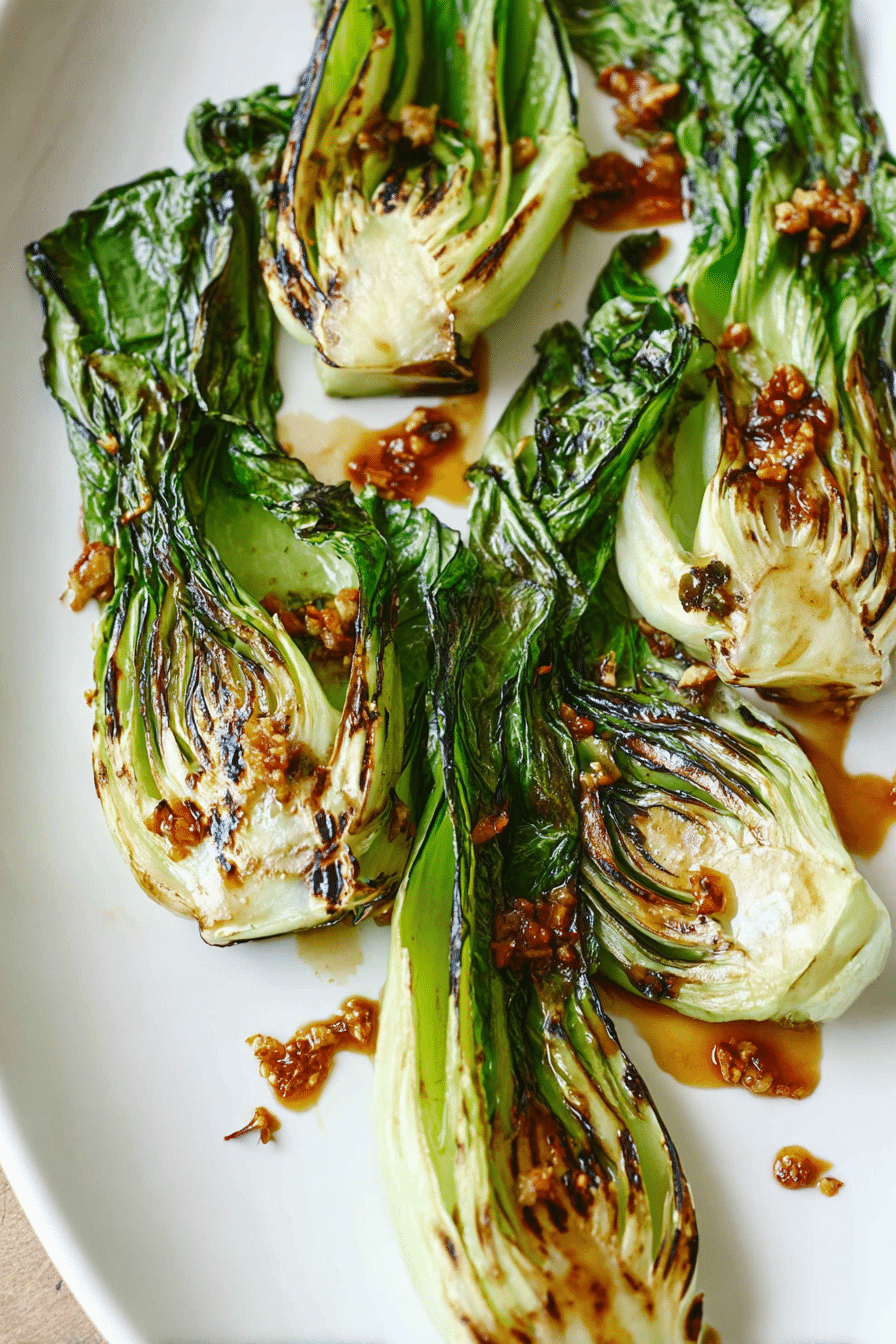 Grilled baby bok choy with ginger chili sauce on a white plate, garnished with fresh herbs.