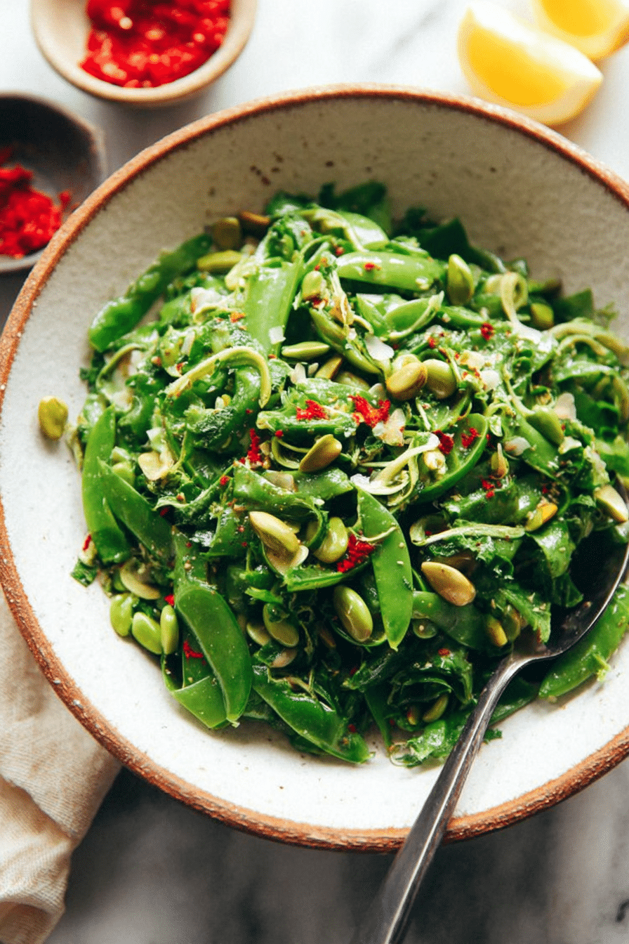 Snap pea salad with zesty lemon vinaigrette garnished with fresh basil and pistachios in a wooden bowl.
