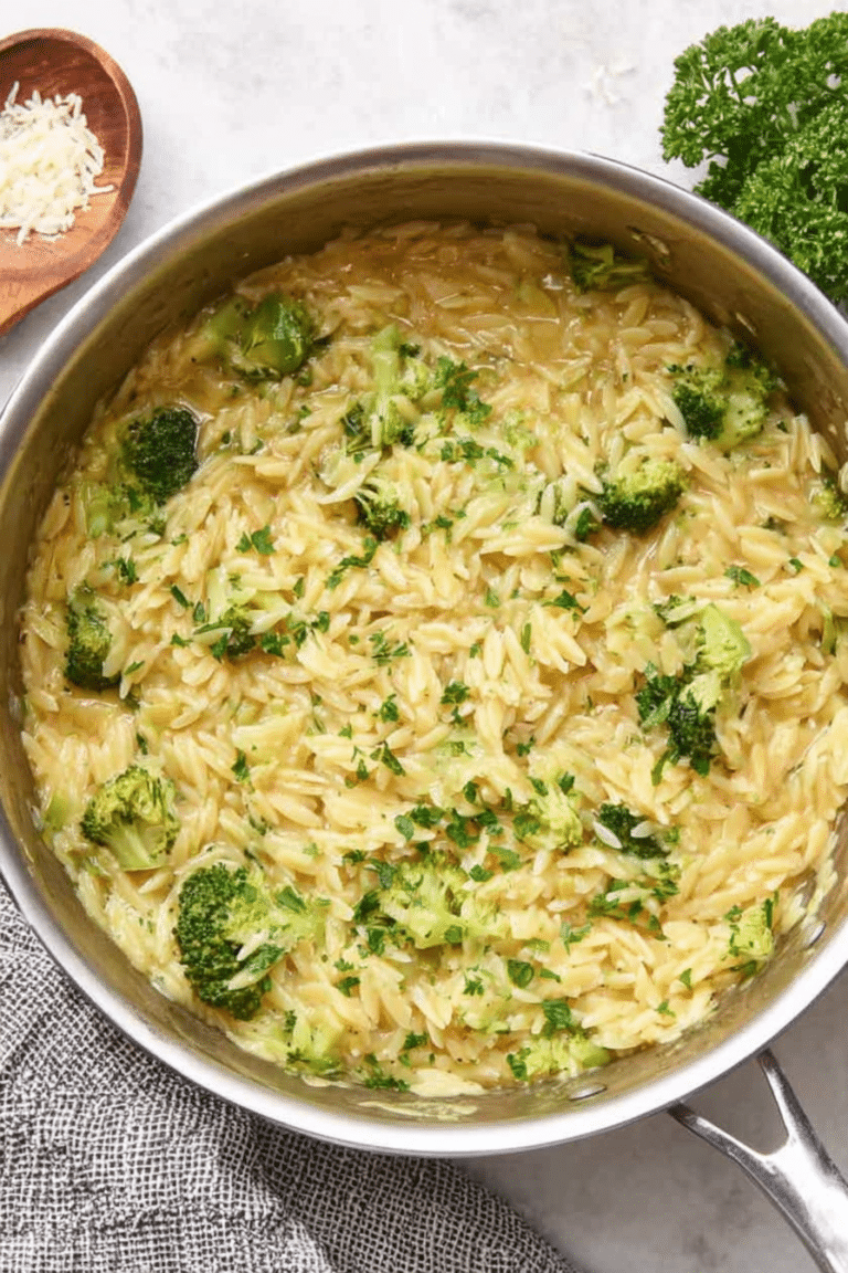 Creamy broccoli cheddar orzo in a bowl, topped with cheese on a wooden table.