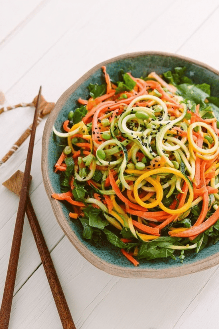 Cold spiralized sesame noodle salad with cucumber, carrot, and zucchini, garnished with sesame seeds on a rustic wooden table.