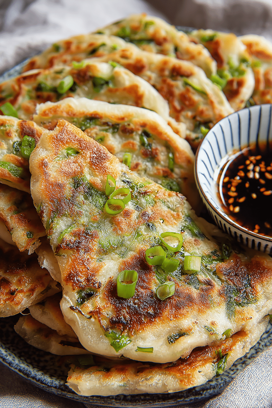 Crispy Chinese scallion pancakes on a plate with dipping sauce and fresh scallions.