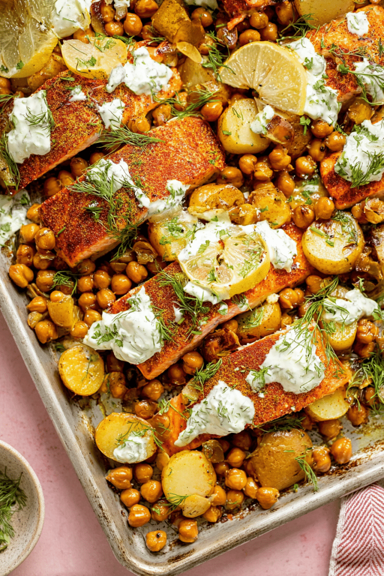 Easy sheet pan salmon dinner with roasted potatoes and chickpeas, garnished with yogurt sauce and herbs.