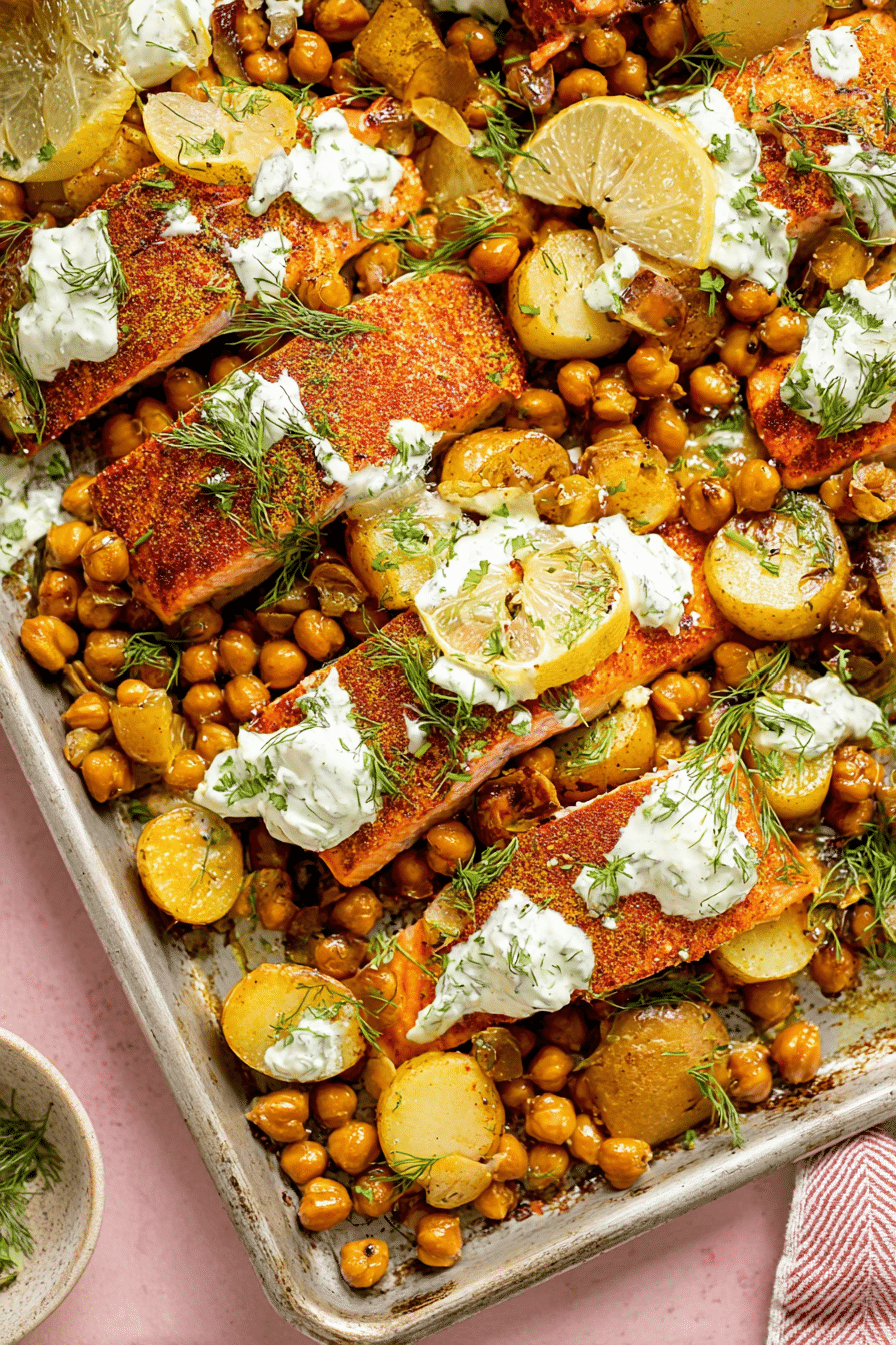 Easy sheet pan salmon dinner with roasted potatoes and chickpeas, garnished with yogurt sauce and herbs.
