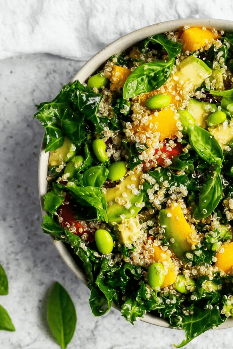 Vibrant kale quinoa salad with avocado, mango, and tomatoes served in a rustic bowl, showcasing healthy ingredients.