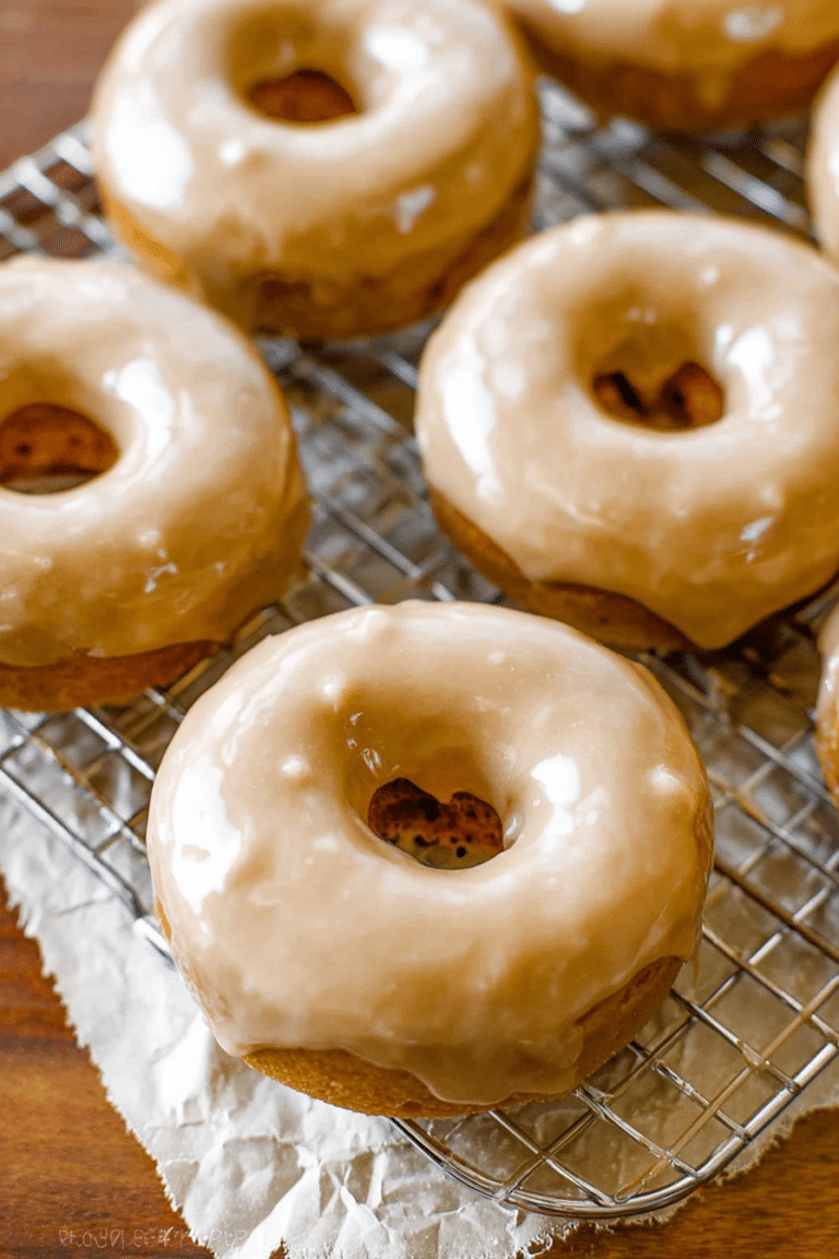Freshly baked maple glazed donuts with a rich glaze on a wooden table, surrounded by maple syrup and spices.