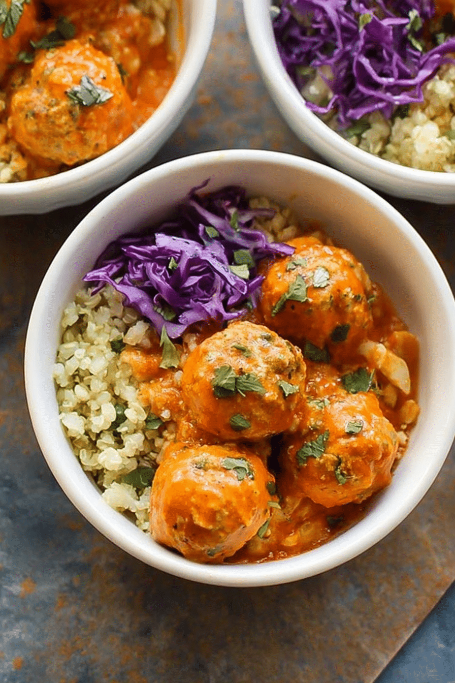 Red coconut curry meatballs on a bed of cauliflower rice with fresh herbs and lime slices