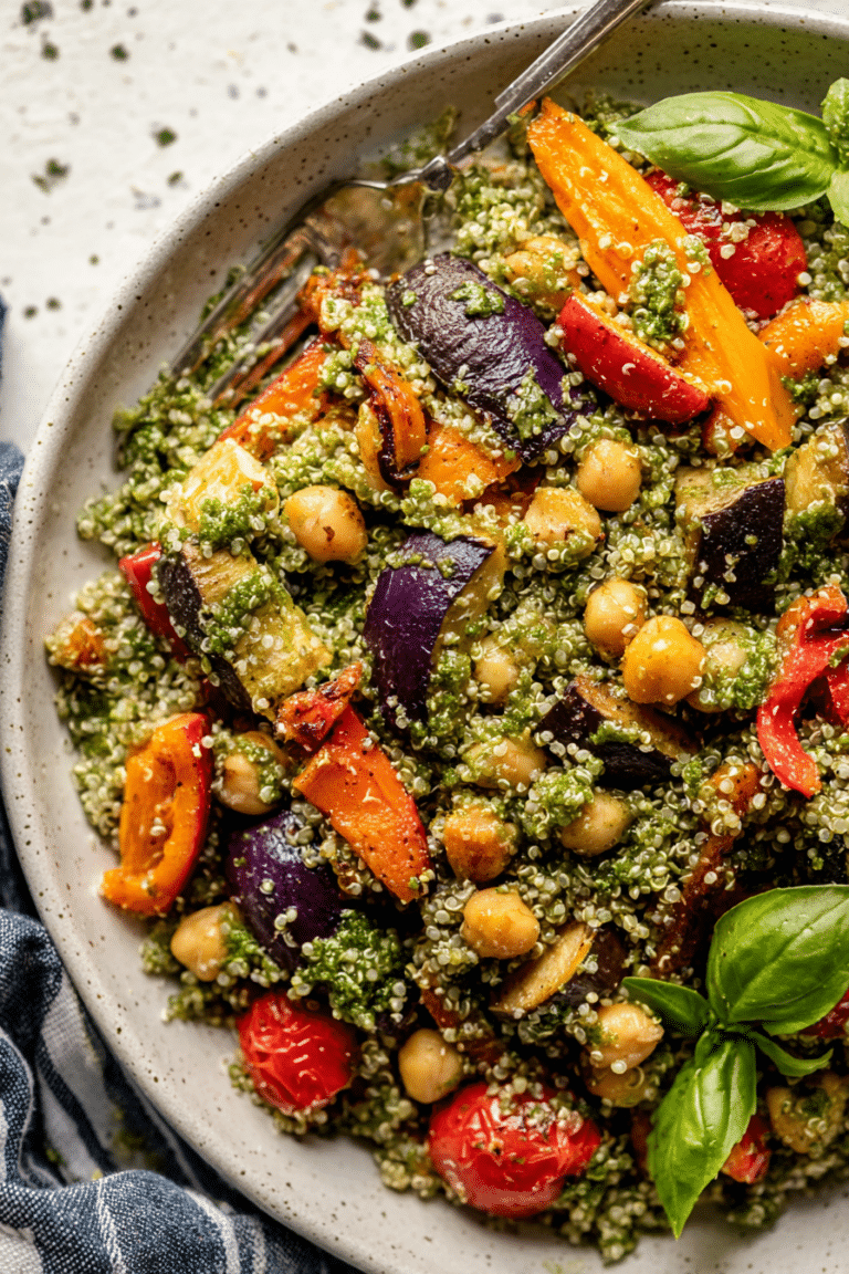 A colorful roasted veggie chickpea pesto quinoa salad with fresh basil, featuring roasted bell peppers, onions, and sweet potatoes, served in a bowl.