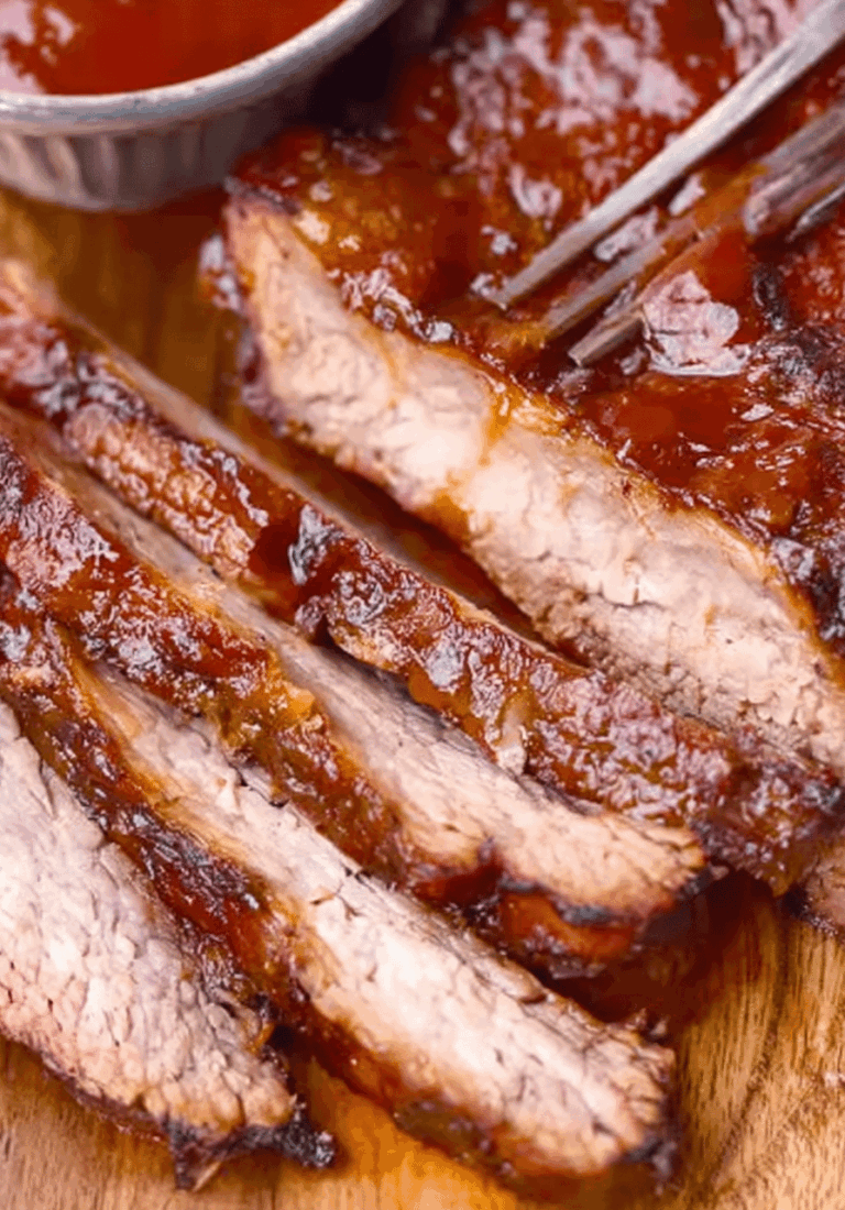 Sliced slow cooker beef brisket on a wooden board with barbecue sauce