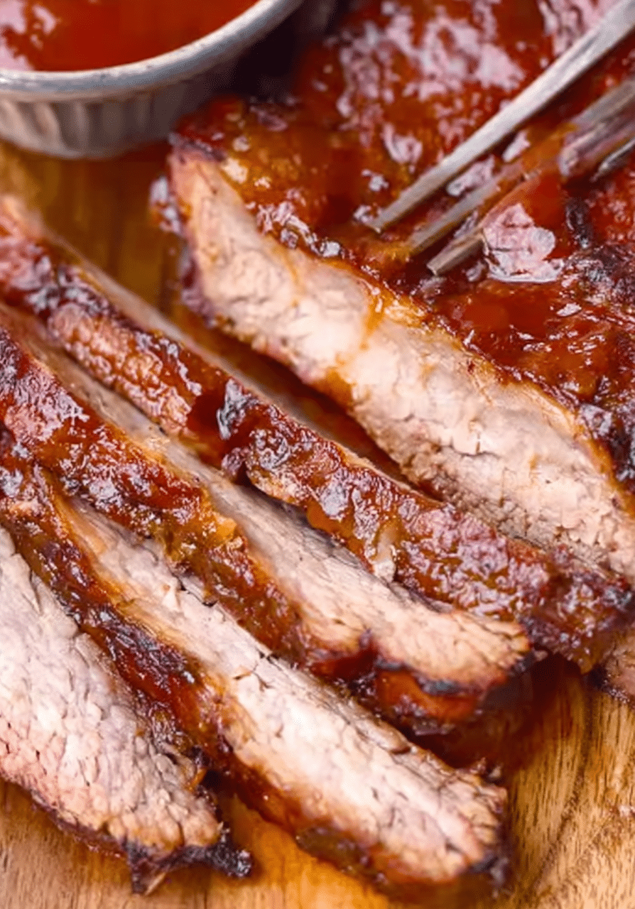 Sliced slow cooker beef brisket on a wooden board with barbecue sauce