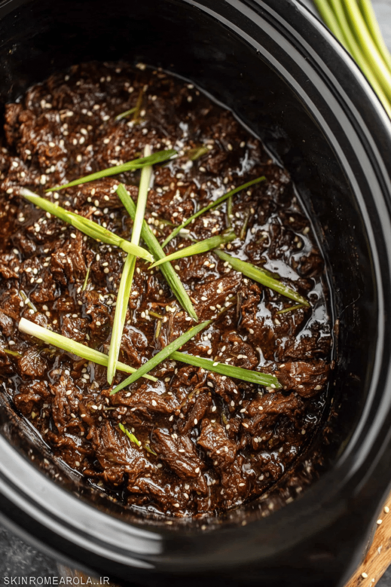 Delicious slow cooker Korean beef over rice, garnished with sesame seeds and green onions, with a side of vegetables.