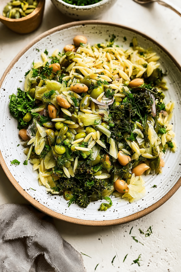 Spring orzo salad with asparagus, olives, and herbs served in a bowl on a wooden table.