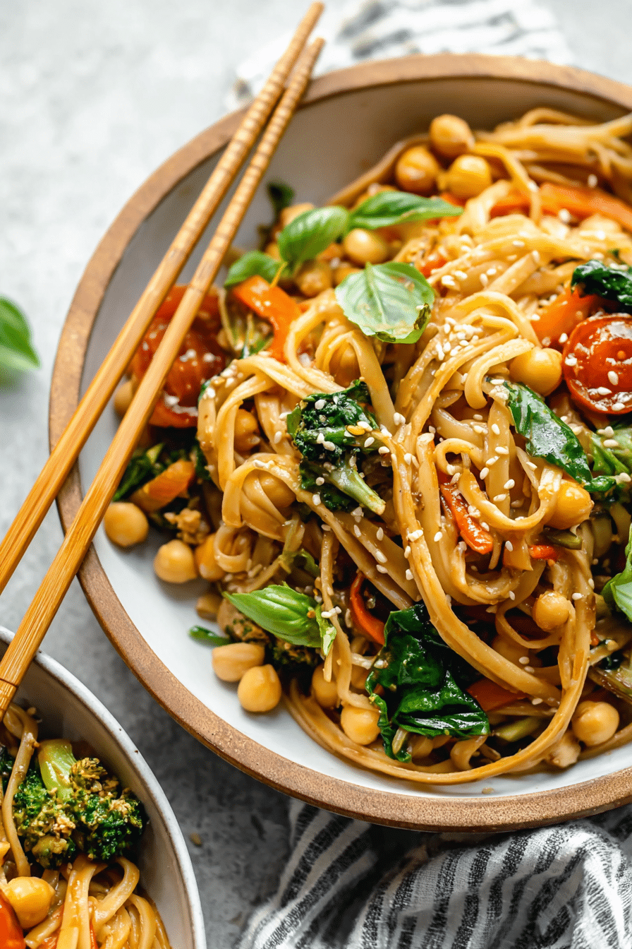 Delicious vegan stir fry sesame noodles served in a bowl with fresh vegetables and garnished with basil leaves and roasted cashews.