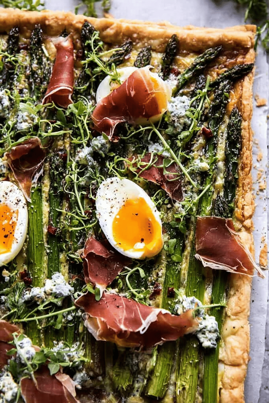 Asparagus, egg, and prosciutto tart garnished with fresh basil, served on a wooden table.