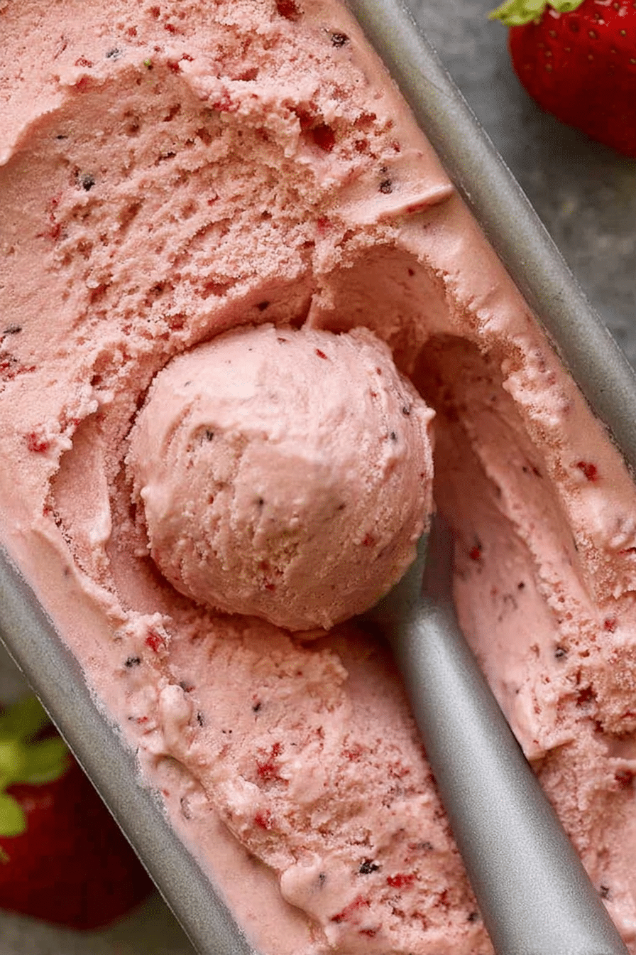 Close-up of creamy strawberry ice cream in a cone, topped with fresh strawberries and mint.