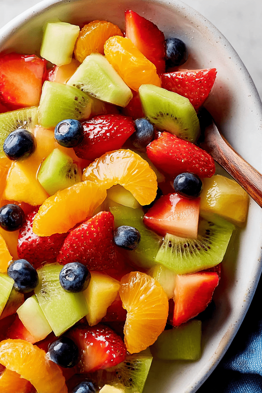 Close-up of a colorful fruit salad featuring pineapple, strawberries, kiwis, grapes, blueberries, and mandarin oranges drizzled with honey-lime dressing.