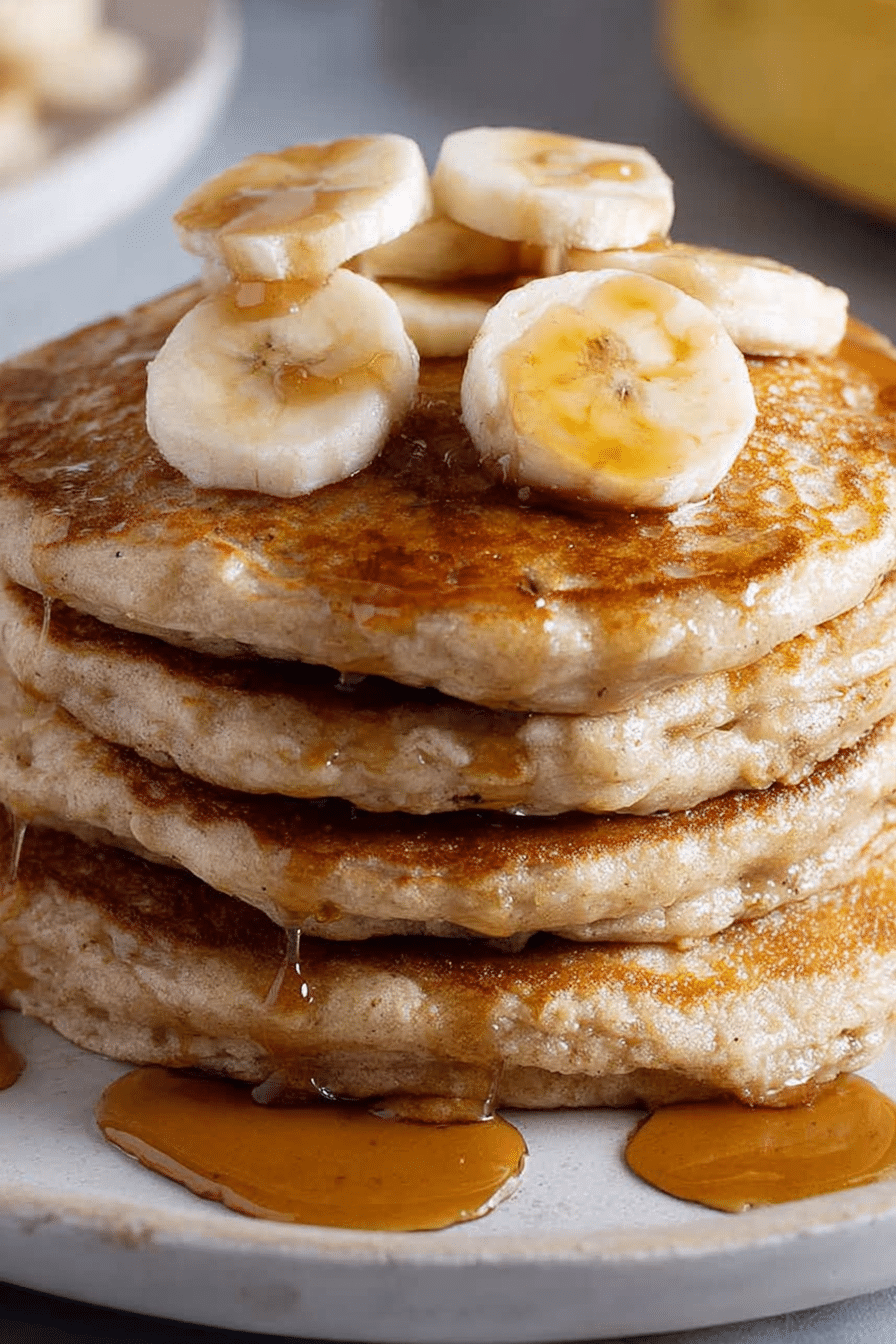 Fluffy banana pancakes stacked high, topped with sliced bananas and maple syrup on a colorful breakfast table.