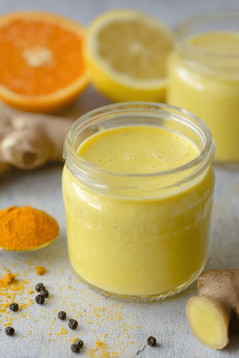 Homemade lemon ginger turmeric shot with fresh lemons, ginger, and turmeric on a wooden table.