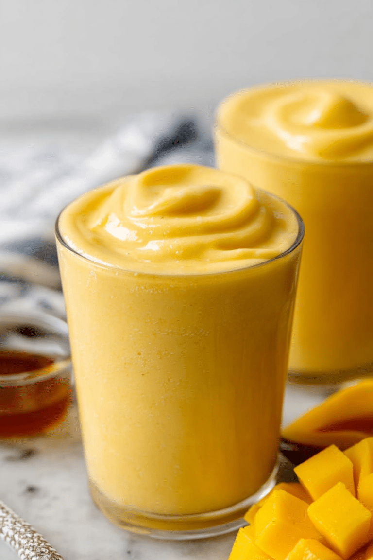A refreshing mango coconut milk smoothie in a glass, garnished with mango slices and mint, ideal for summer.