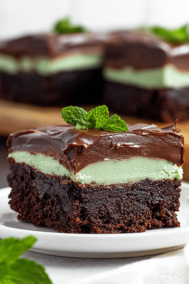 Close-up of sliced mint chocolate brownie topped with mint leaves and chocolate ganache on wooden table