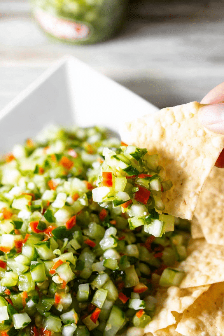 A vibrant bowl of Pickle de Gallo with tortilla chips, featuring fresh cucumbers, red bell peppers, dill pickles, and onions.