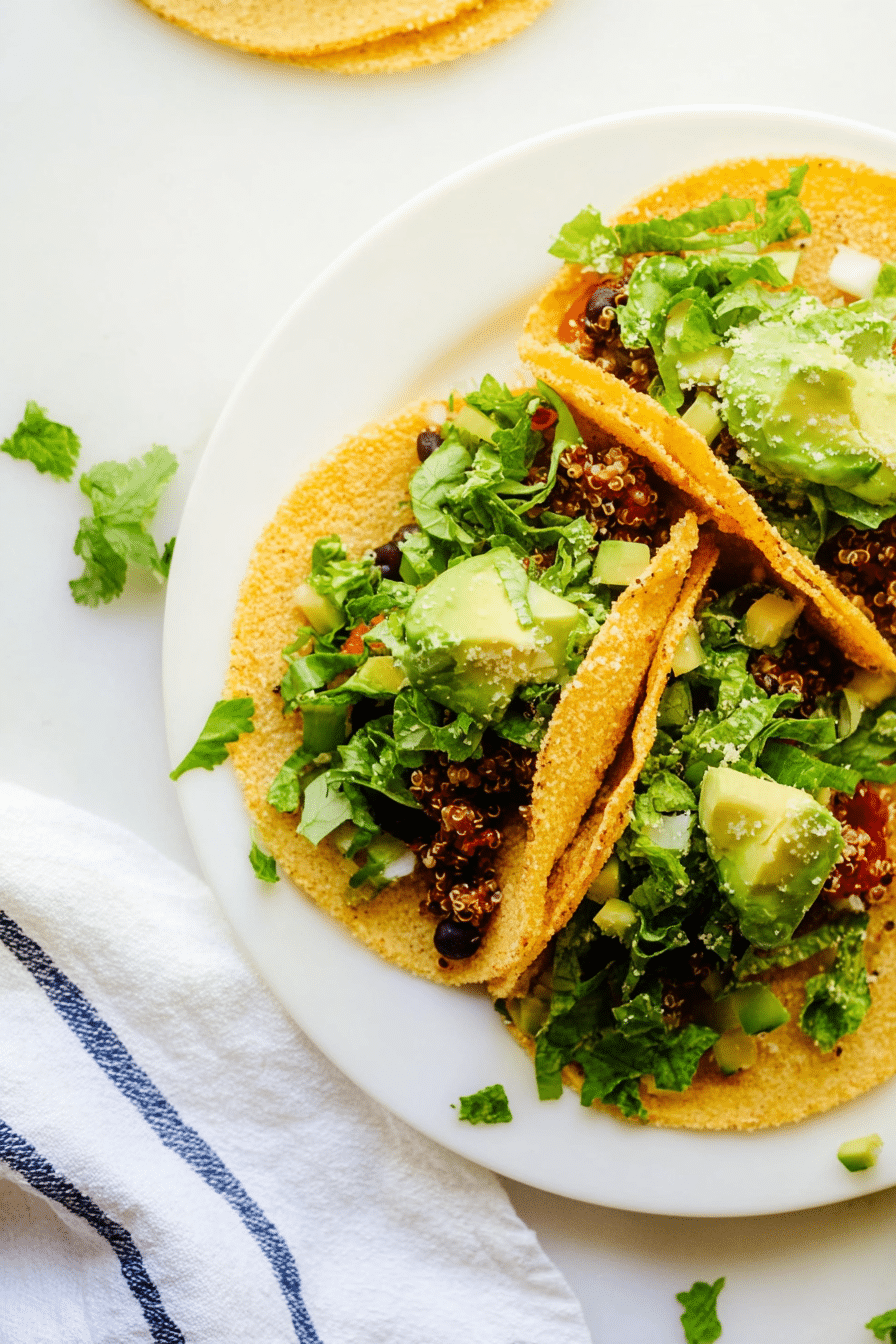 A colorful close-up of quinoa black bean tacos topped with avocado sauce and cilantro, highlighting vibrant ingredients.