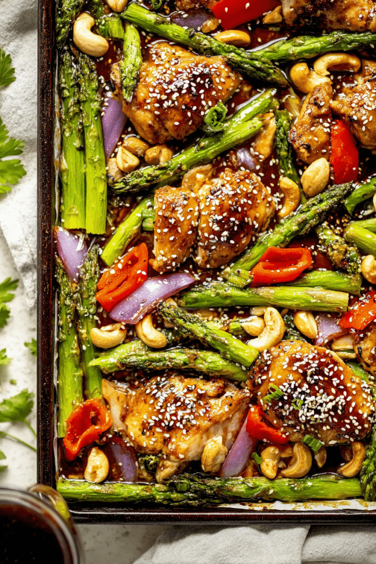 Overhead view of sheet pan sesame chicken with colorful vegetables and sesame seeds garnished with fresh herbs.