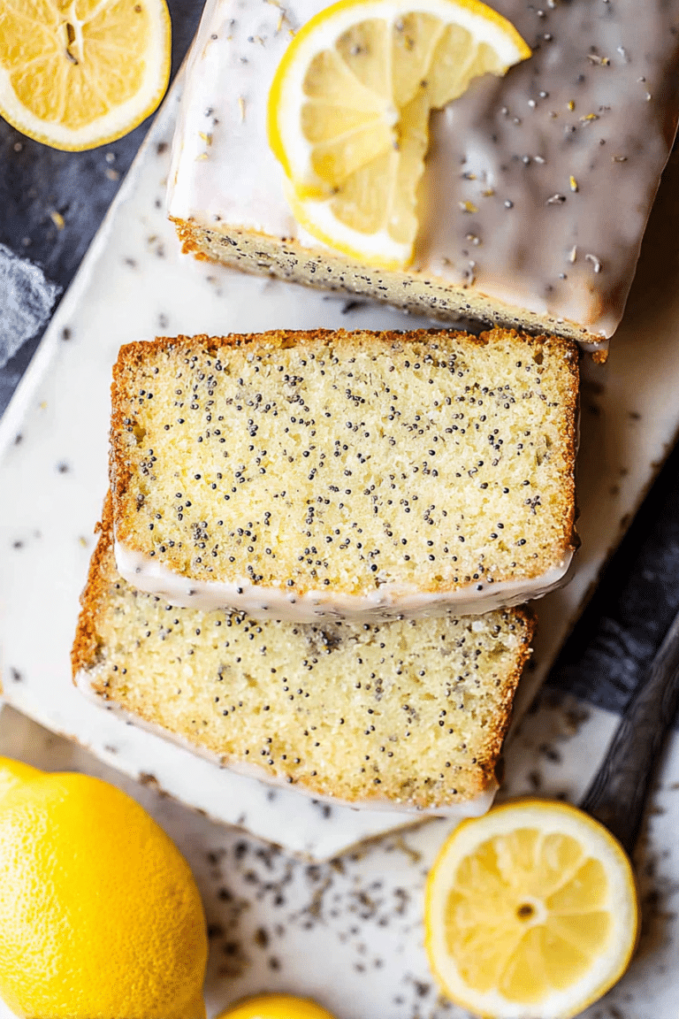 Sliced lemon poppy seed loaf on a cutting board with lemons and mint.
