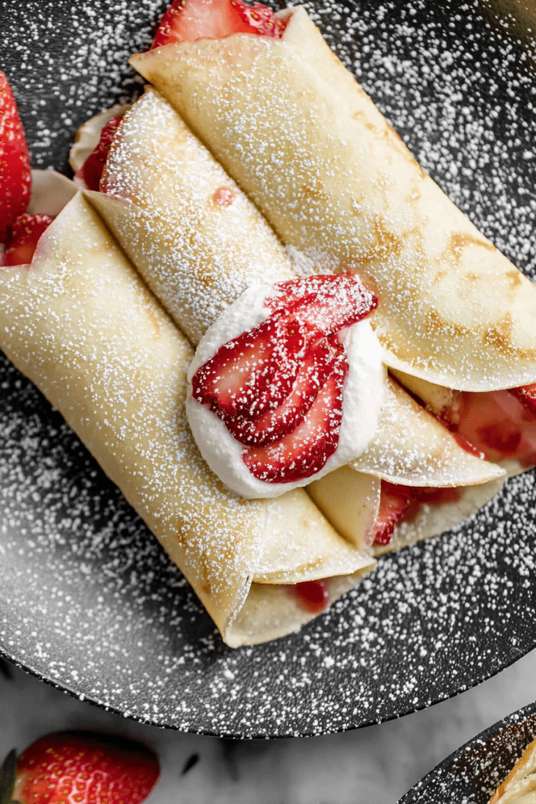 Delicious strawberry crepes topped with whipped cream and fresh strawberries, garnished with powdered sugar.