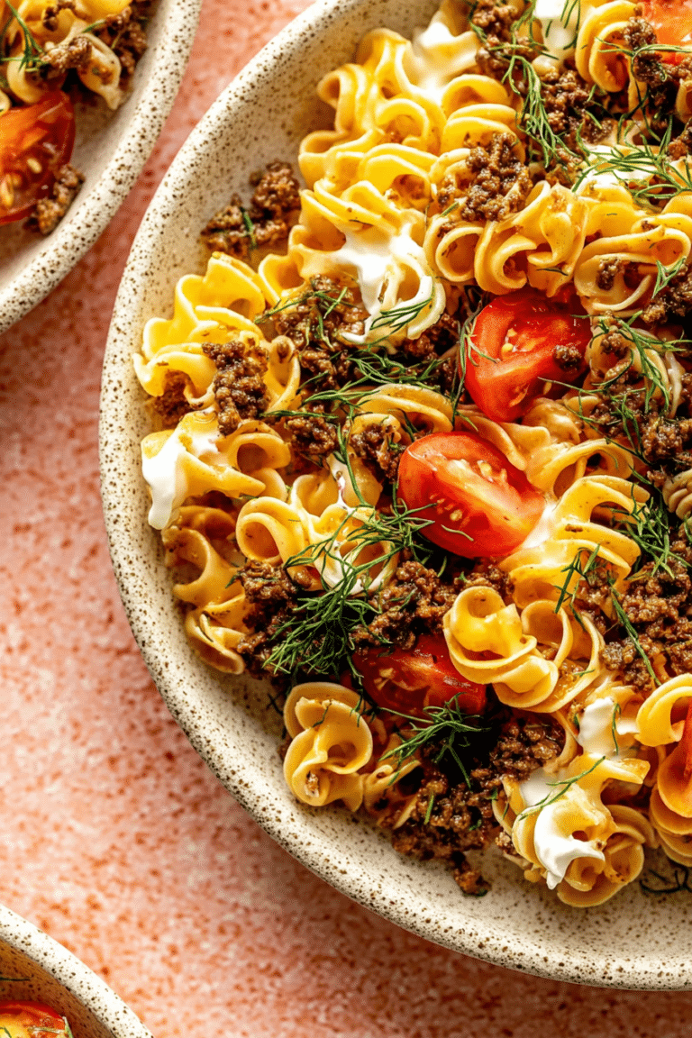 Delicious viral Turkish pasta topped with creamy garlic yogurt sauce, ground beef, and cherry tomatoes, garnished with fresh herbs.