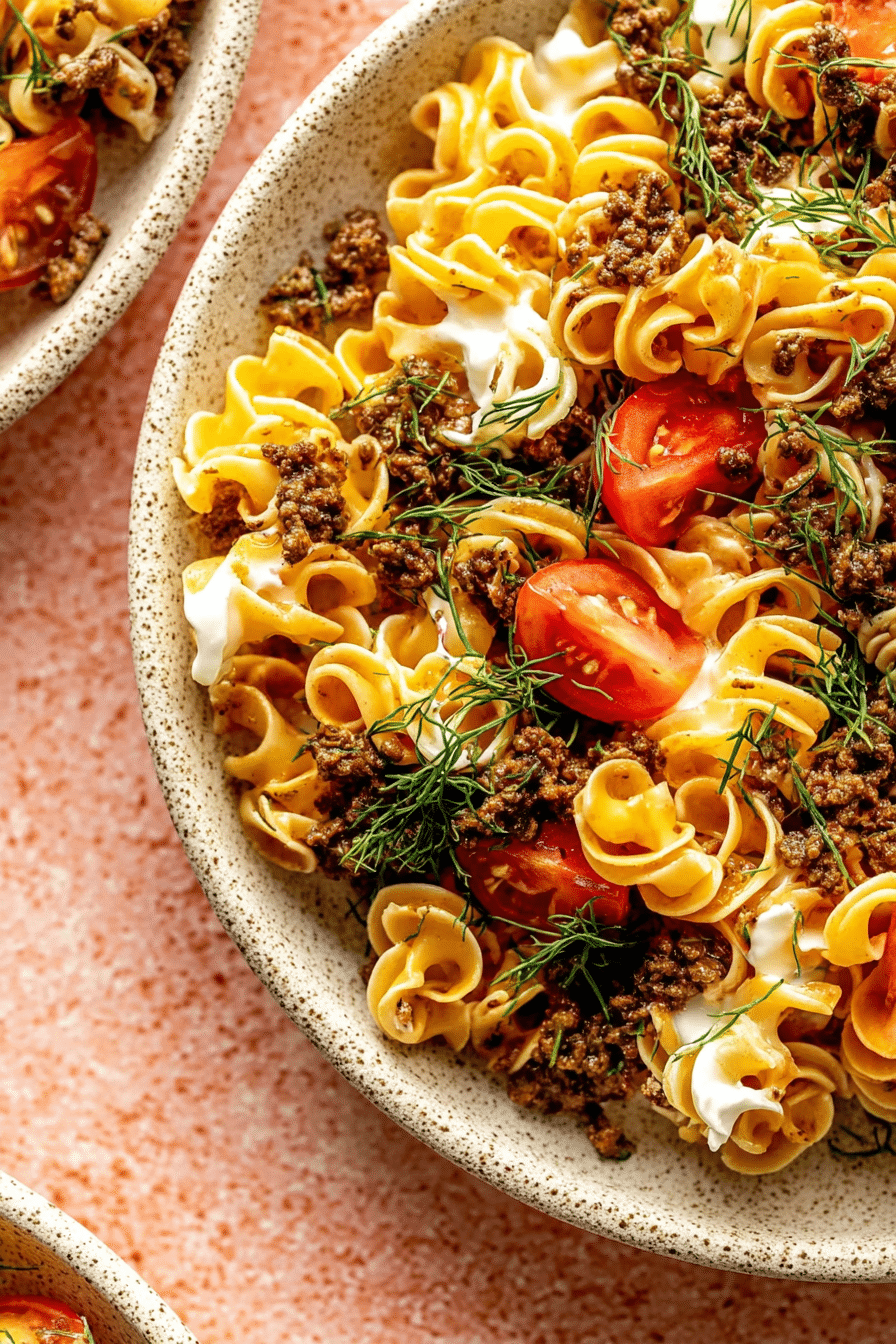 Delicious viral Turkish pasta topped with creamy garlic yogurt sauce, ground beef, and cherry tomatoes, garnished with fresh herbs.