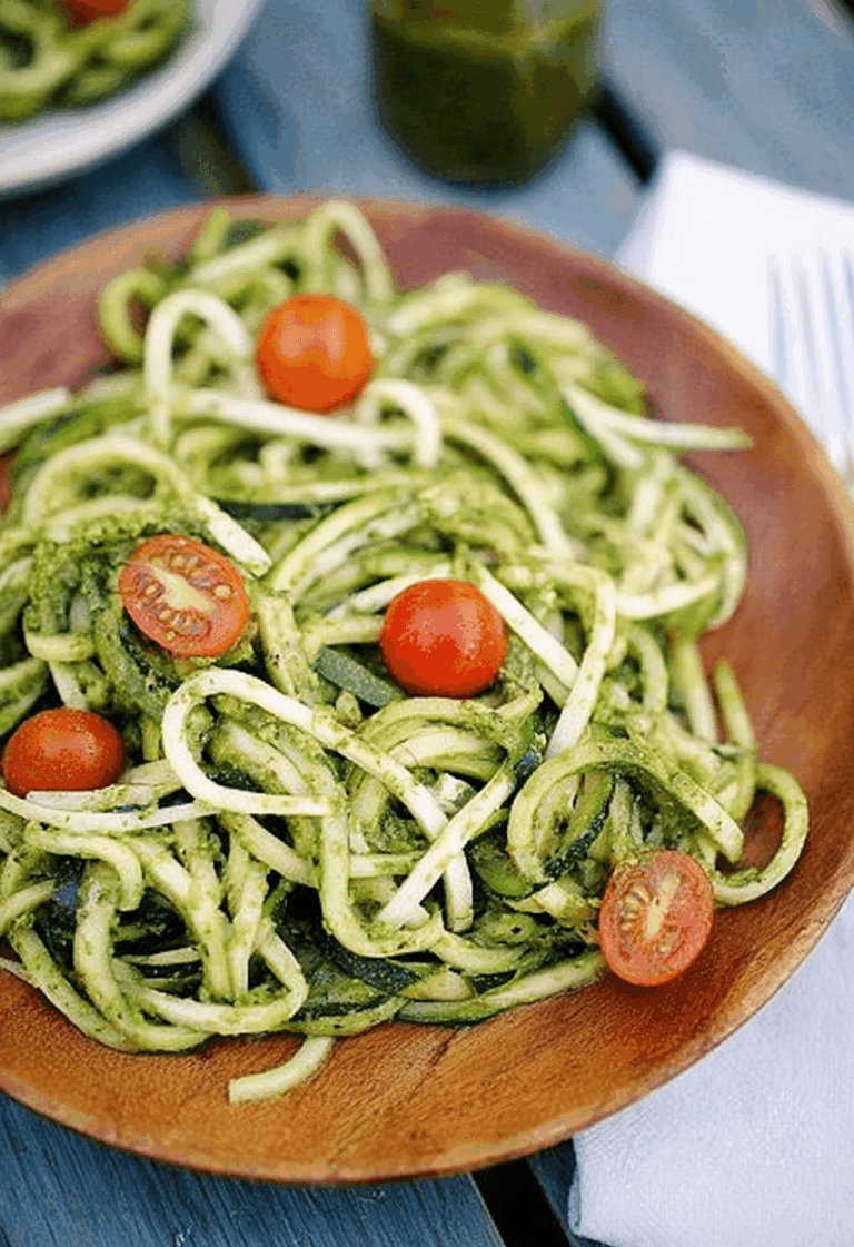 Bowl of zucchini noodles with pesto and cherry tomatoes on a wooden table