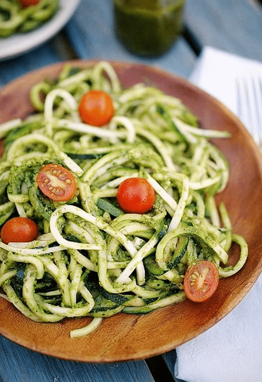 Bowl of zucchini noodles with pesto and cherry tomatoes on a wooden table