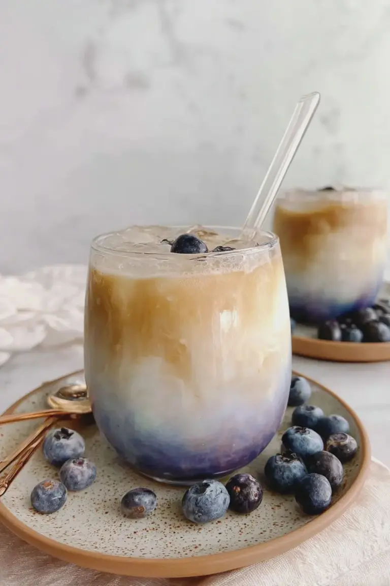 Blueberry latte in a glass with whipped cream and blueberries on a rustic wooden table