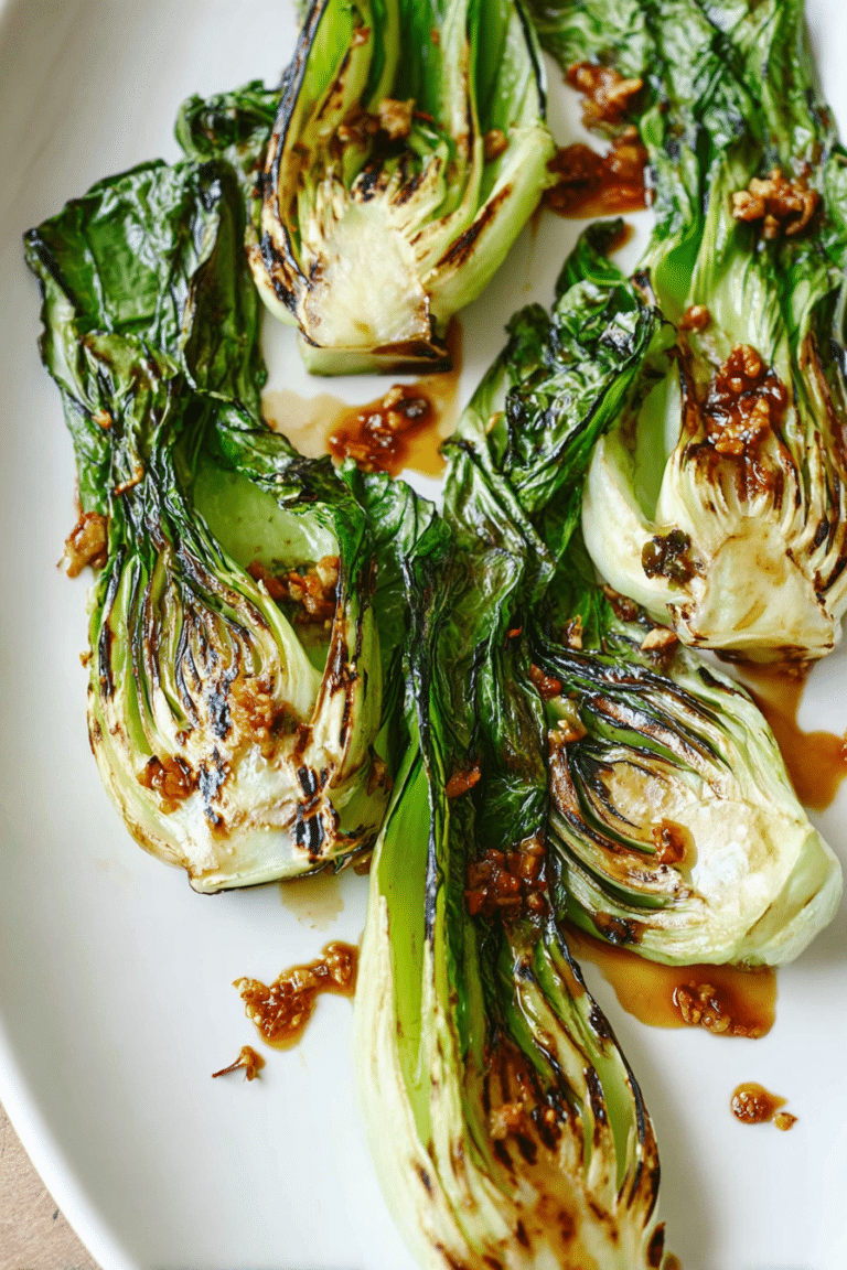 Grilled baby bok choy with ginger chili sauce on a white plate, garnished with fresh herbs.