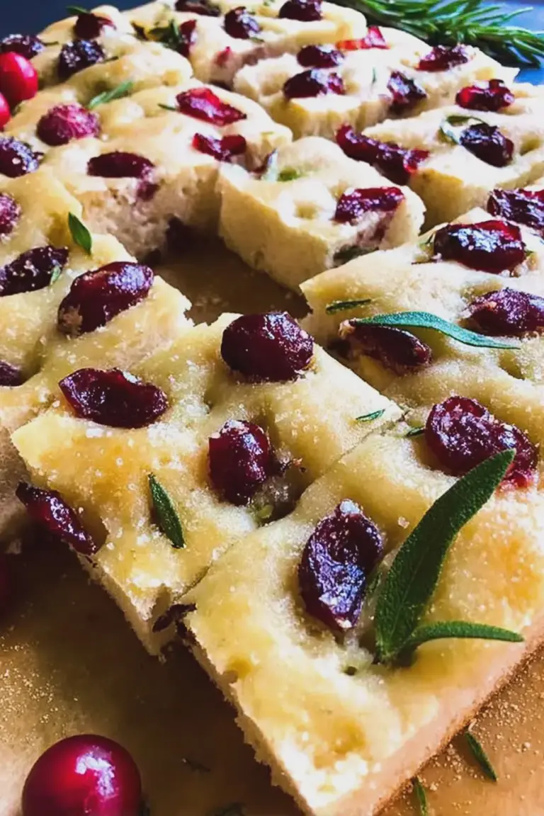 Freshly baked rosemary cherry focaccia bread topped with cherries and rosemary on a wooden table
